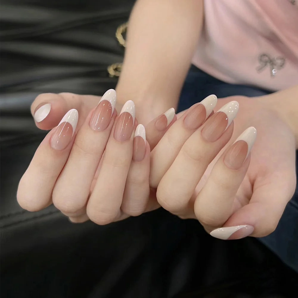 Close-up of hands showcasing almond-shaped false nails with a French tip design, featuring a gradient transition from white to nude pink and beige.